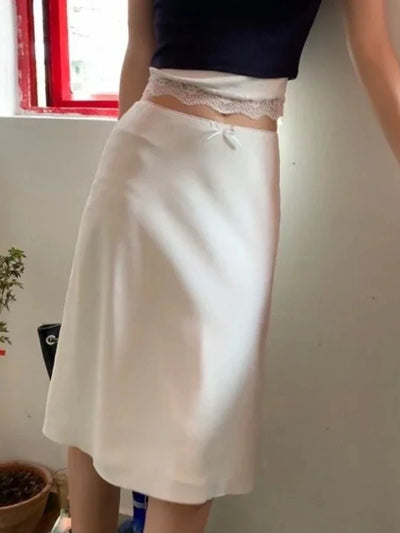 Close-up side angle of white satin midi skirt lace waistband and bow, crop top styling
