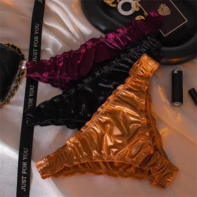 Three satin panties in burgundy, black, and gold arranged on white satin