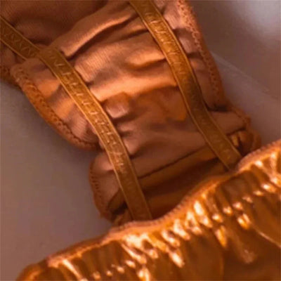 Macro close-up of tonal woven elastic waistband on gold satin panties