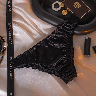Black gathered satin bikini panties with ruched edges on white satin background
