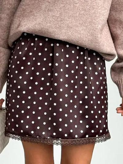 Woman wearing brown polka dot mini skirt with lace hem, white sweater, and black knee-high boots