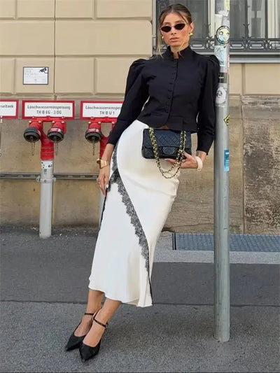 Full-length street style shot of woman in ivory lace midi skirt paired with black fitted top and strappy heels
