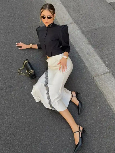 Overhead view of woman lying on pavement wearing ivory satin skirt with diagonal black lace trim and stilettos