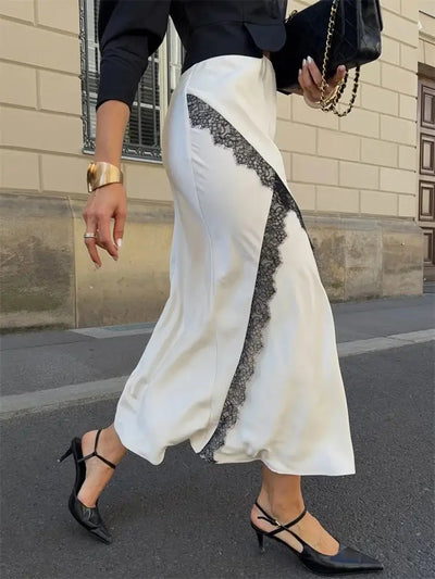 Side street-style walking shot focusing on fluid ivory satin skirt with diagonal black lace panel detail