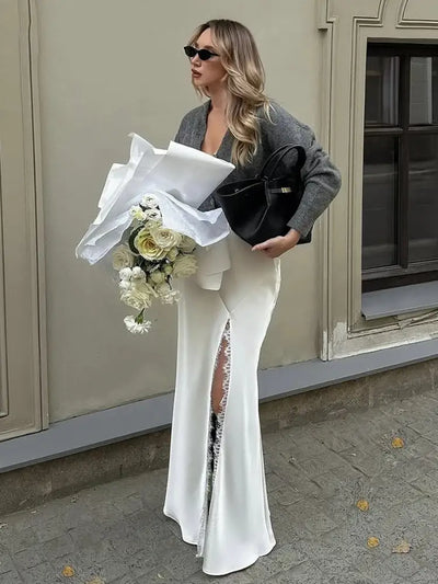 Woman in white satin mermaid skirt holding white roses and black bag outdoors