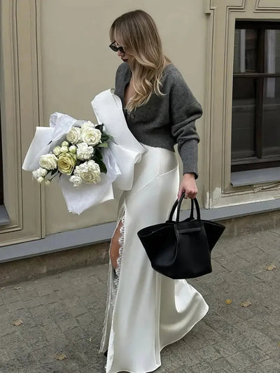 Woman walking in white satin mermaid skirt with lace slit and black tote bag