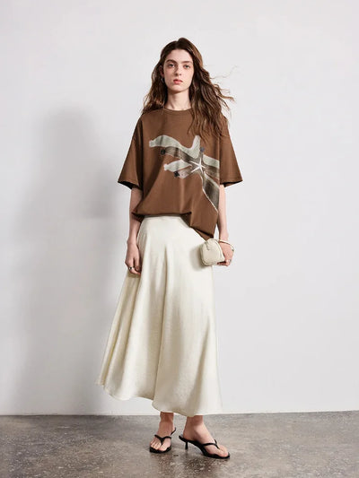 Full outfit view, ivory satin midi skirt paired with brown graphic tee and small bag