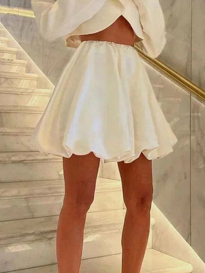 Side view of ivory satin bubble-hem mini skirt with elastic waist, glossy finish visible