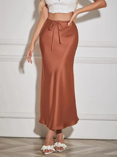 Front view of a terracotta satin maxi skirt with bow-tied drawstring waist and white crop top