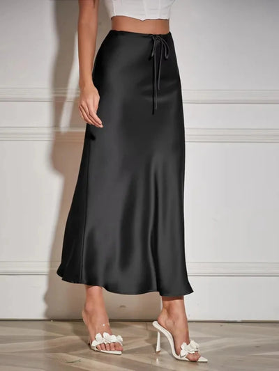 Black high-shine maxi skirt with drawstring waist worn with white crop top and heeled mules