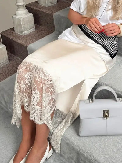 Seated view of ivory lace-hem satin midi skirt with gray top-handle bag beside white flats