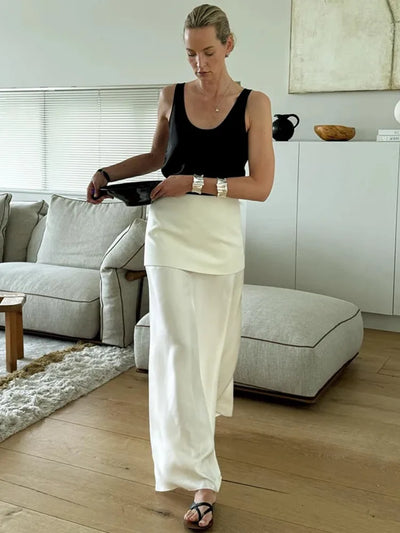 Woman in white high-waist maxi skirt lifting upper layer panel indoors in modern living room