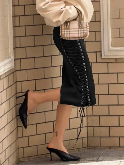 Side view of black satin lace-up midi skirt with visible grommet detail, paired with black pointed-toe mules