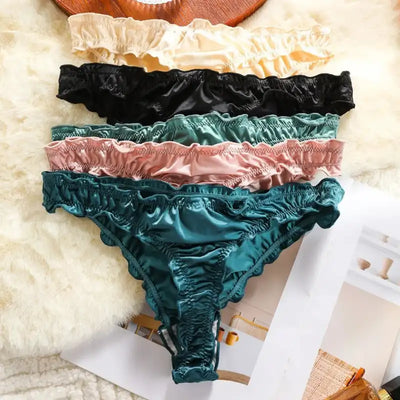 Five satin thong panties in ivory, black, teal, blush, and dark green laid flat on fur