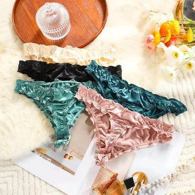 Four satin thong panties fanned out on fur, showing ruffled edges in teal, blush, black, and ivory
