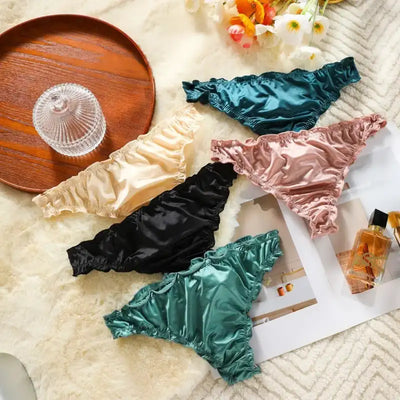 Five satin thong panties spread in a circle on fur, showing back cut in multiple colors