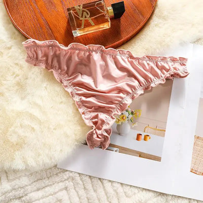 Single blush pink satin thong with ruffled edges on fur surface next to wooden tray