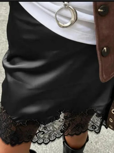 Close-up of black glossy mini skirt with wide black floral lace hem trim, styled with white tee and brown jacket