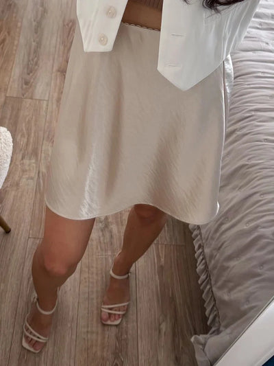 Overhead view of champagne crinkled satin mini skirt with white vest and strappy sandals on wood floor