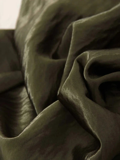 Close-up of olive green crinkled satin fabric with deep folds and high-shine finish