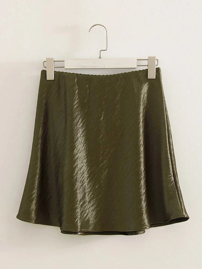 Olive green crinkled satin A-line mini skirt hanging on a hanger against a white wall