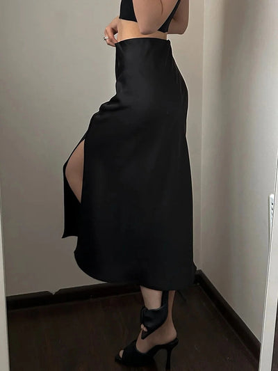 Black satin midi skirt with deep side slit, worn with black heels and bra top, side view