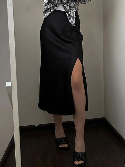 Black satin midi skirt with side slit, styled with knotted plaid shirt and black slide sandals