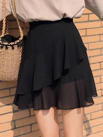 Back view of black tiered ruffle mini skirt paired with beige top and woven straw bag