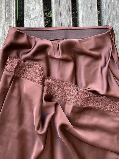 Close-up flat lay of brown satin skirt showing tone-on-tone lace hem detail and back zip closure