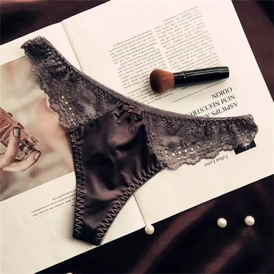 Charcoal gray satin thong panties with lace trim and small satin bow, flat lay on open magazine