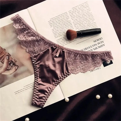 Dusty mauve satin thong panties with wide lace sides and bow, flat lay on magazine with makeup brush