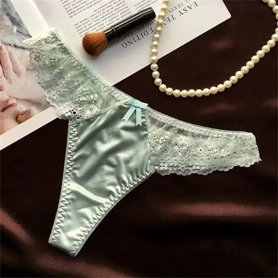Mint green satin thong panties with lace sides and bow detail, styled with pearl necklace and makeup brush