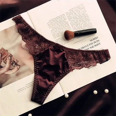 Dark chocolate brown satin thong panties with floral lace waistband, flat lay on magazine with makeup brush