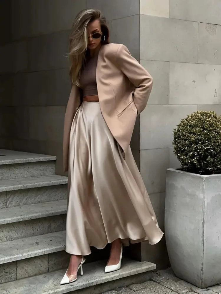 Woman in champagne satin midi skirt and blush blazer posed on stone steps looking down