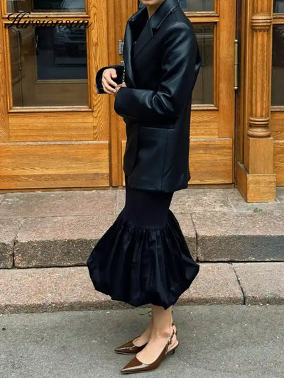 Side profile of woman in black bubble-hem midi skirt styled with oversized black leather blazer and brown slingback heels