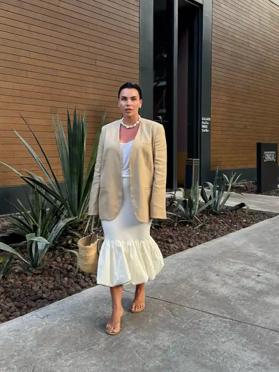 Woman in ivory bubble-hem midi skirt with beige blazer, white tank, and straw bag near agave plants