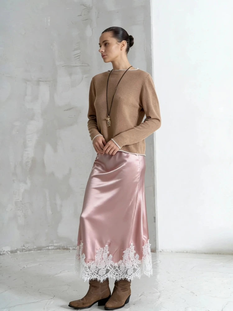 Woman wearing a pink satin midi skirt with white lace hem and camel sweater with ankle boots