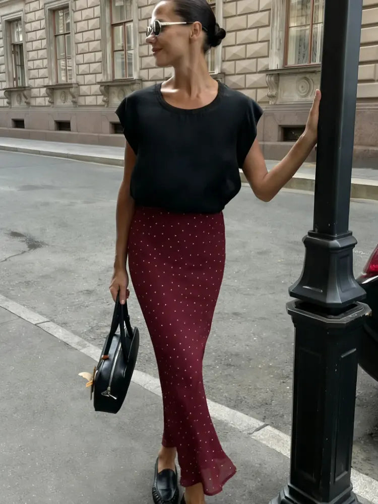 Woman wearing a burgundy polka dot midi satin skirt with black tee and loafers on a city street