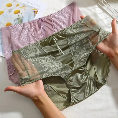 Two hands holding sage green and lavender floral lace satin panties on white background