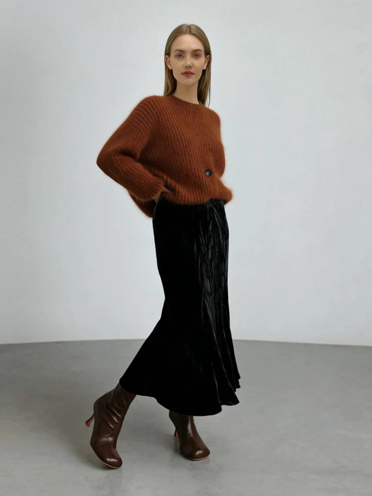 Model wearing a black crinkled velvet midi skirt with a rust ribbed sweater and brown heeled boots