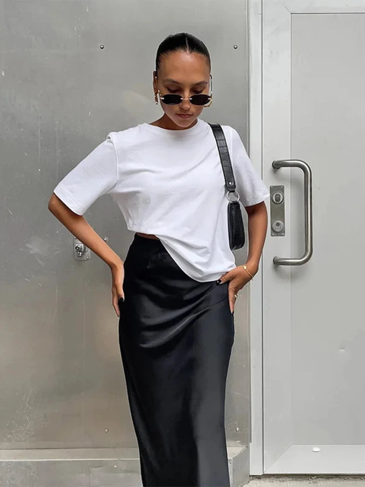 Woman wearing relaxed black midi satin skirt with white tee and crossbody bag outdoors