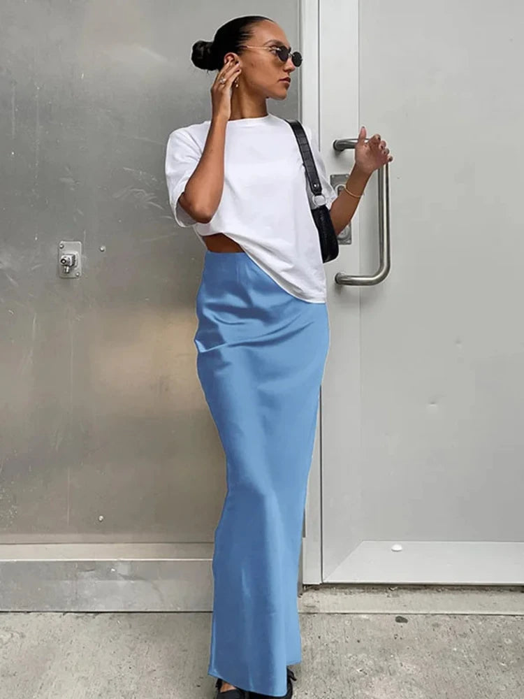 Woman wearing a sky blue maxi satin skirt with white tee and crossbody bag outdoors