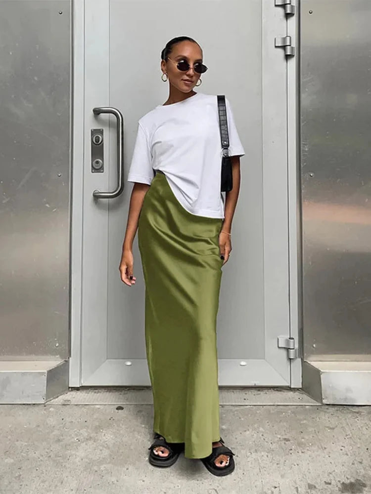 Woman wearing an olive green high-waist satin maxi skirt with a white t-shirt and black sandals
