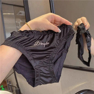 Hands holding black ruched satin Dimple panties showing waistband and leg finish detail in mirror
