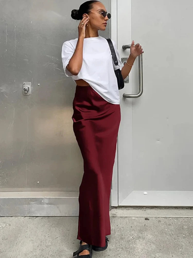 Woman wearing a burgundy high-waist satin maxi skirt with a side slit and white tee