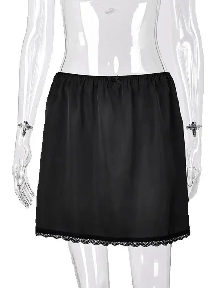 Woman wearing black satin mini skirt with elastic waist, lace-trimmed hem, paired with gray tank top