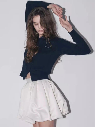 Model wearing navy cropped cardigan and white satin balloon-hem mini skirt, three-quarter pose