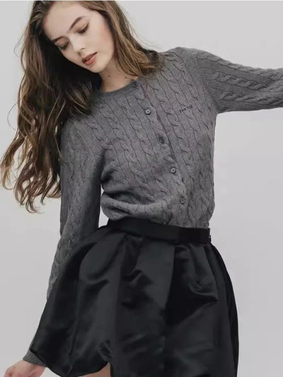 Woman wearing gray cable-knit cardigan with black satin bubble-hem mini skirt, looking down
