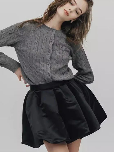 Close-up of gray cable-knit cardigan paired with black satin mini skirt, model smiling