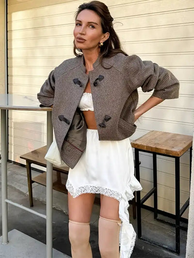 Woman in white asymmetric satin mini skirt with lace ruffle, brown tweed toggle jacket, and knee-high beige boots outdoors